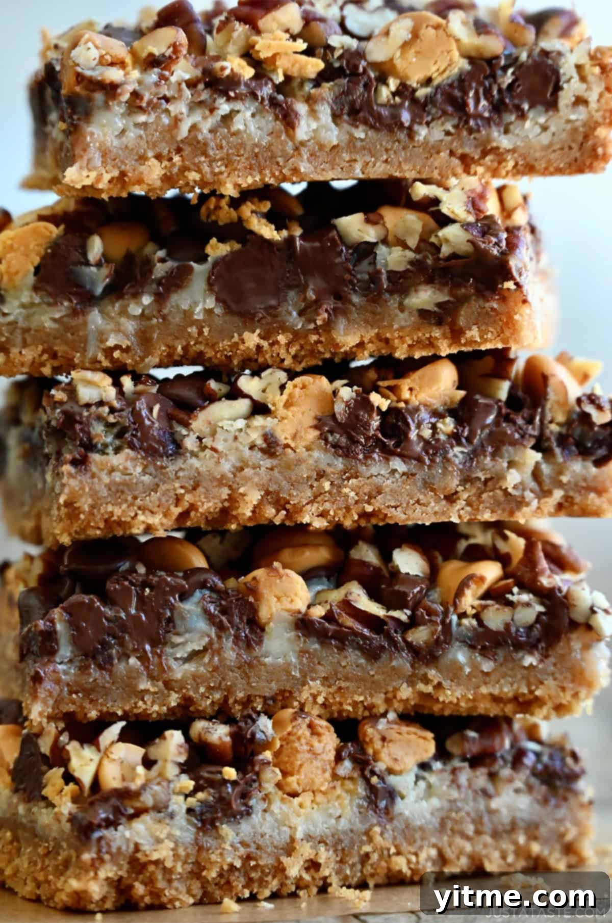 Everything Cookie Bars 14 A tall stack of magic cookie bars made with a graham cracker crust, flaked coconut, butterscotch chips, chocolate chips and chopped pecans, showcasing their delicious layers and generous toppings.