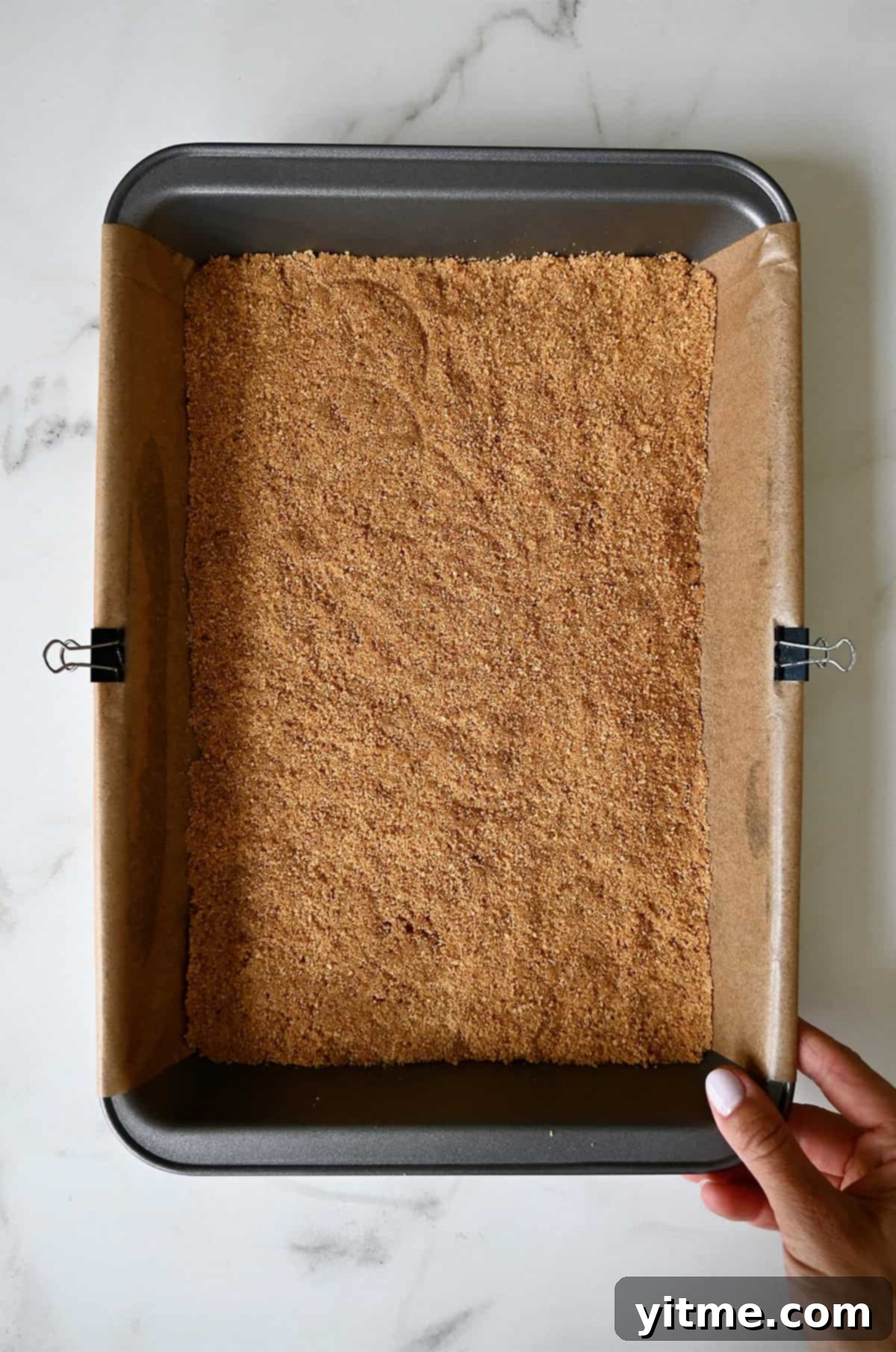 Everything Cookie Bars 8 A perfectly pressed graham cracker crust in a parchment paper-lined 9x13 baking pan, ready for the next layers.