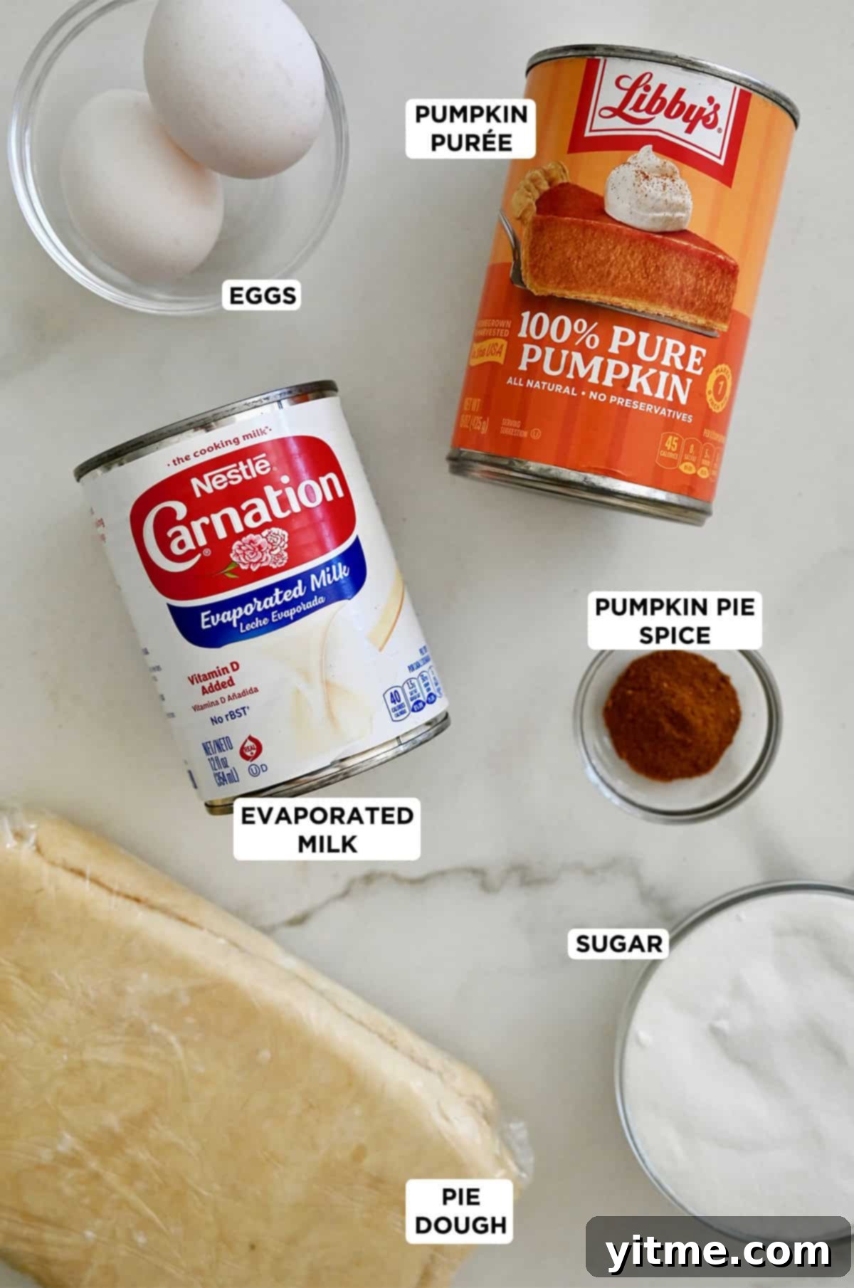 Golden Pumpkin Perfection 4 A selection of essential pumpkin pie ingredients laid out: a can of pumpkin purée, evaporated milk, a jar of pumpkin pie spice, granulated sugar, whole eggs, and an unbaked pie crust.