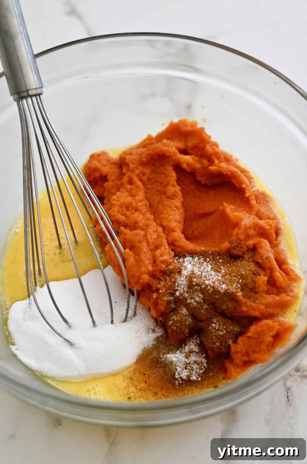 Golden Pumpkin Perfection 6 A glass bowl filled with orange pumpkin puree, seasoned with a generous amount of pumpkin spice, white sugar, and eggs, waiting to be mixed into the pie filling.