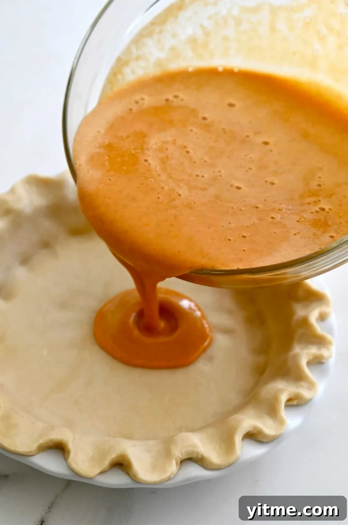Golden Pumpkin Perfection 8 Smooth, creamy pumpkin pie filling being carefully poured from a large glass bowl into an unbaked deep dish pie crust.