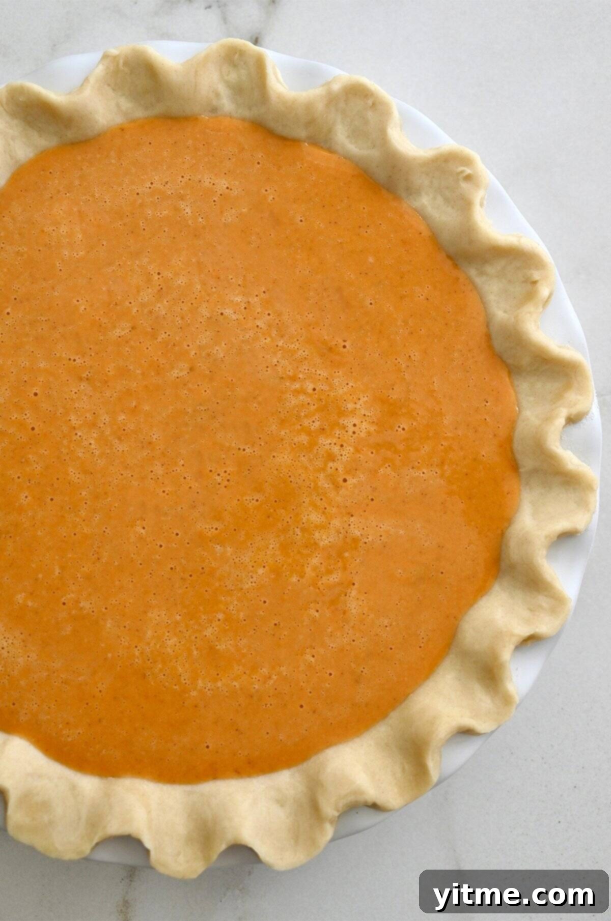Golden Pumpkin Perfection 9 An unbaked pumpkin pie, with its smooth, vibrant orange filling nestled in a deep dish pie pan with a fluted crust, perfectly ready to be placed in the oven.