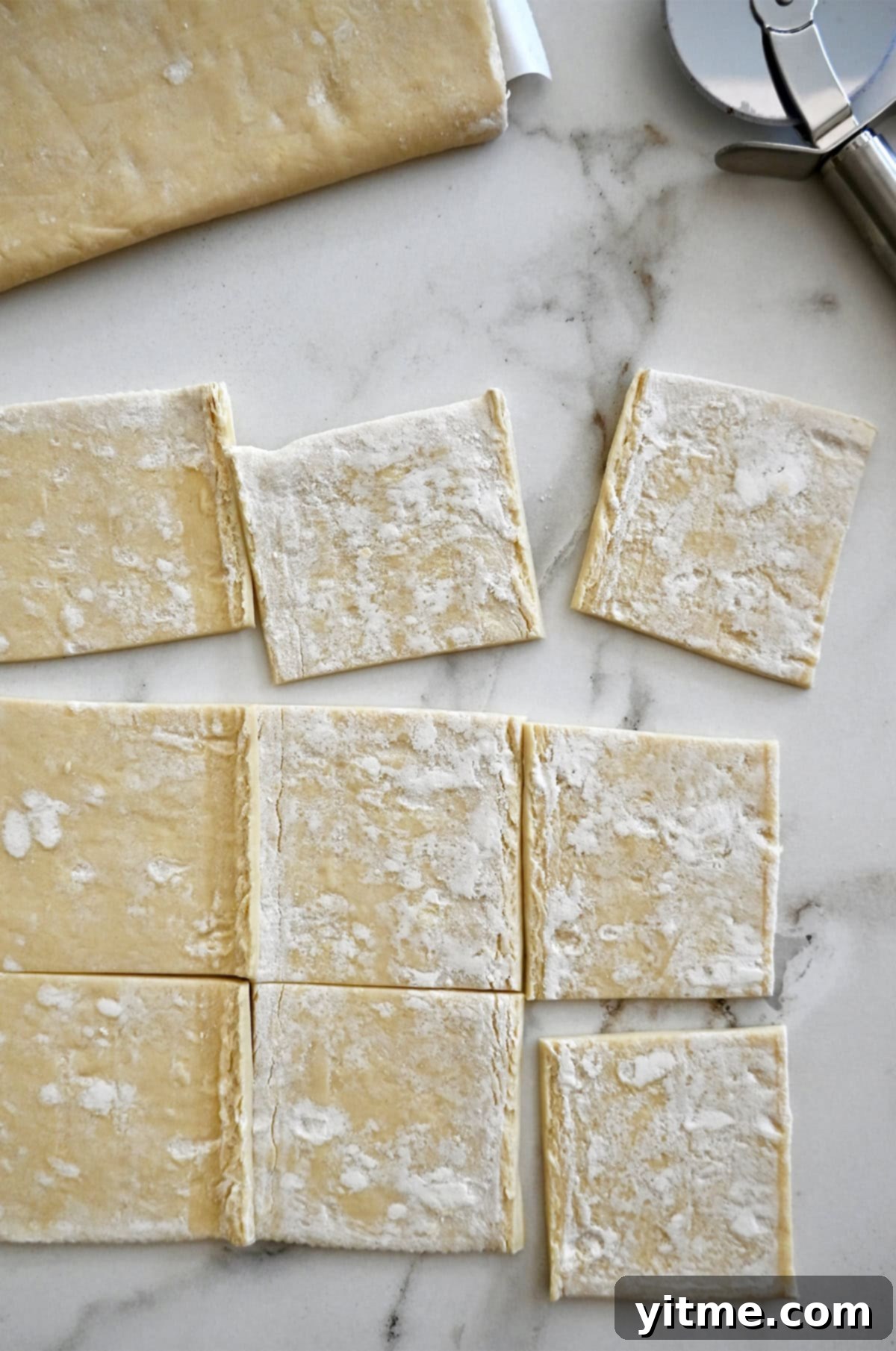 A sheet of puff pastry neatly cut into nine squares on a lightly floured countertop, ready for the next step.