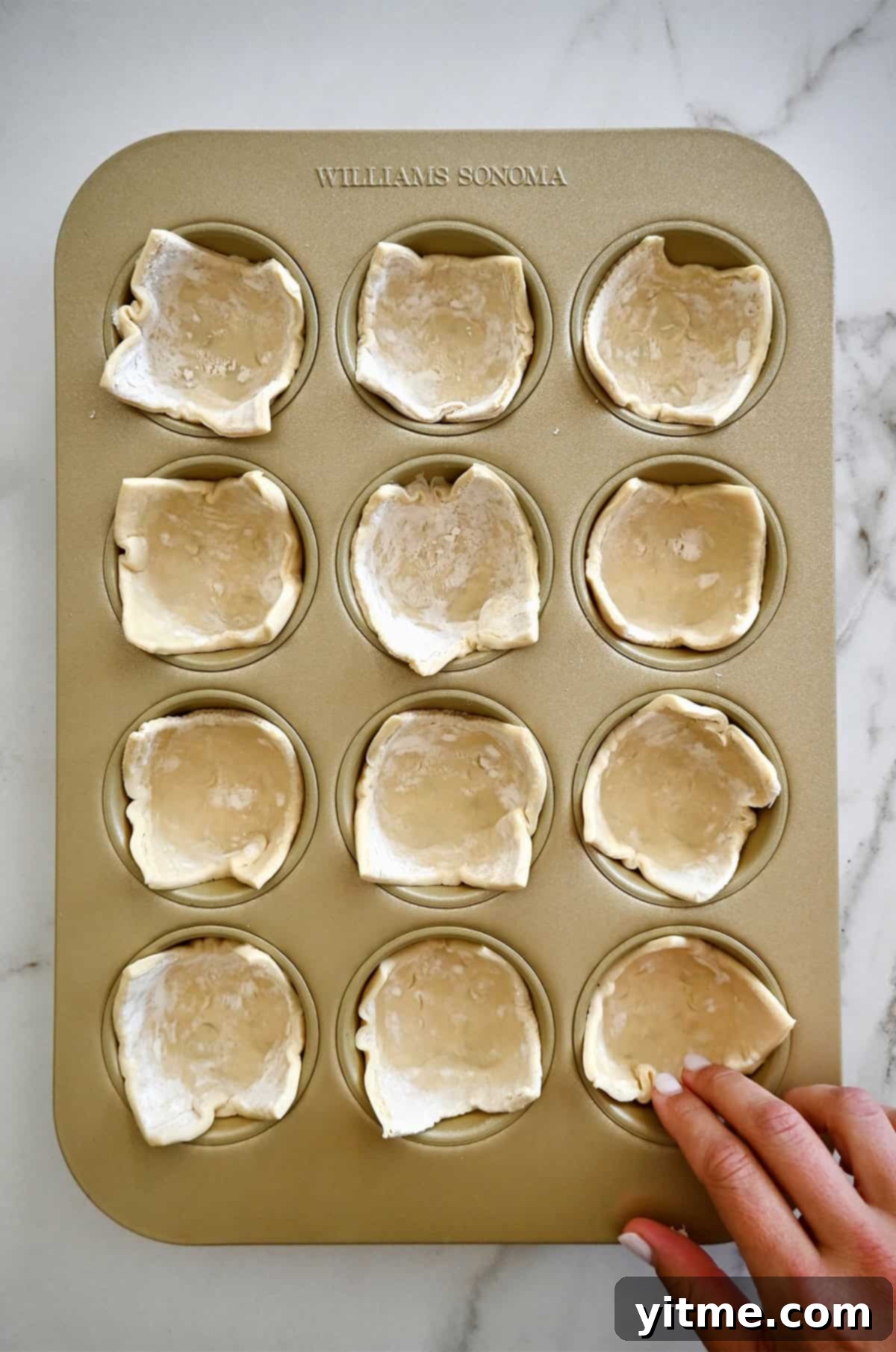 Individual squares of puff pastry gently pressed into each cup of a standard 12-cup muffin pan, forming the base for mini quiches.