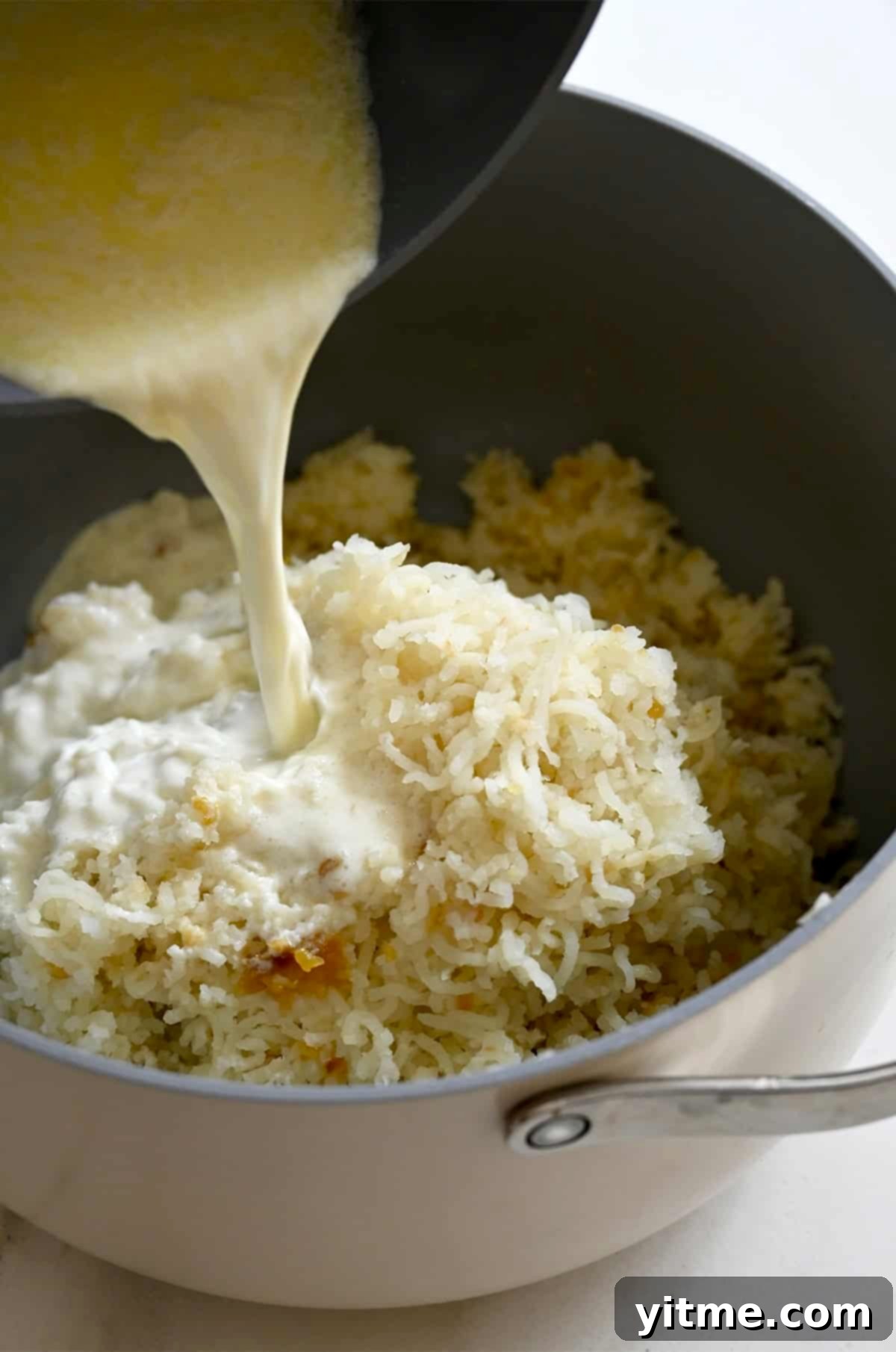 Slowly adding warmed milk and heavy cream to the mashed potatoes.
