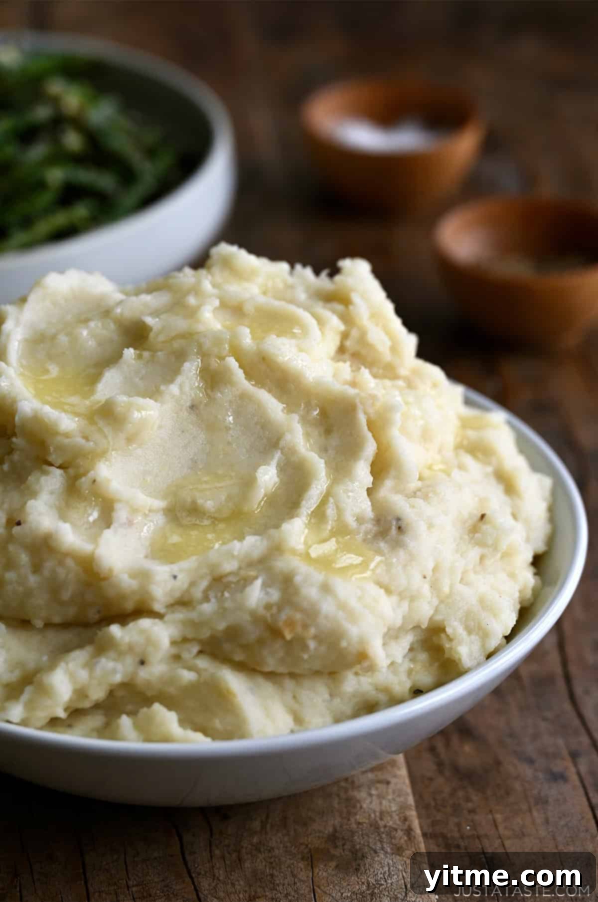 Roasted garlic mashed potatoes topped with melted butter in a white serving bowl.