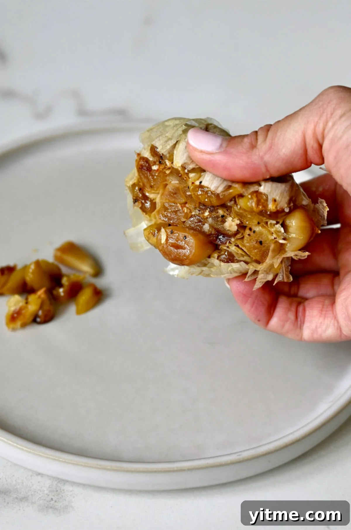 Squeezing roasted garlic cloves from the peels onto a plate.
