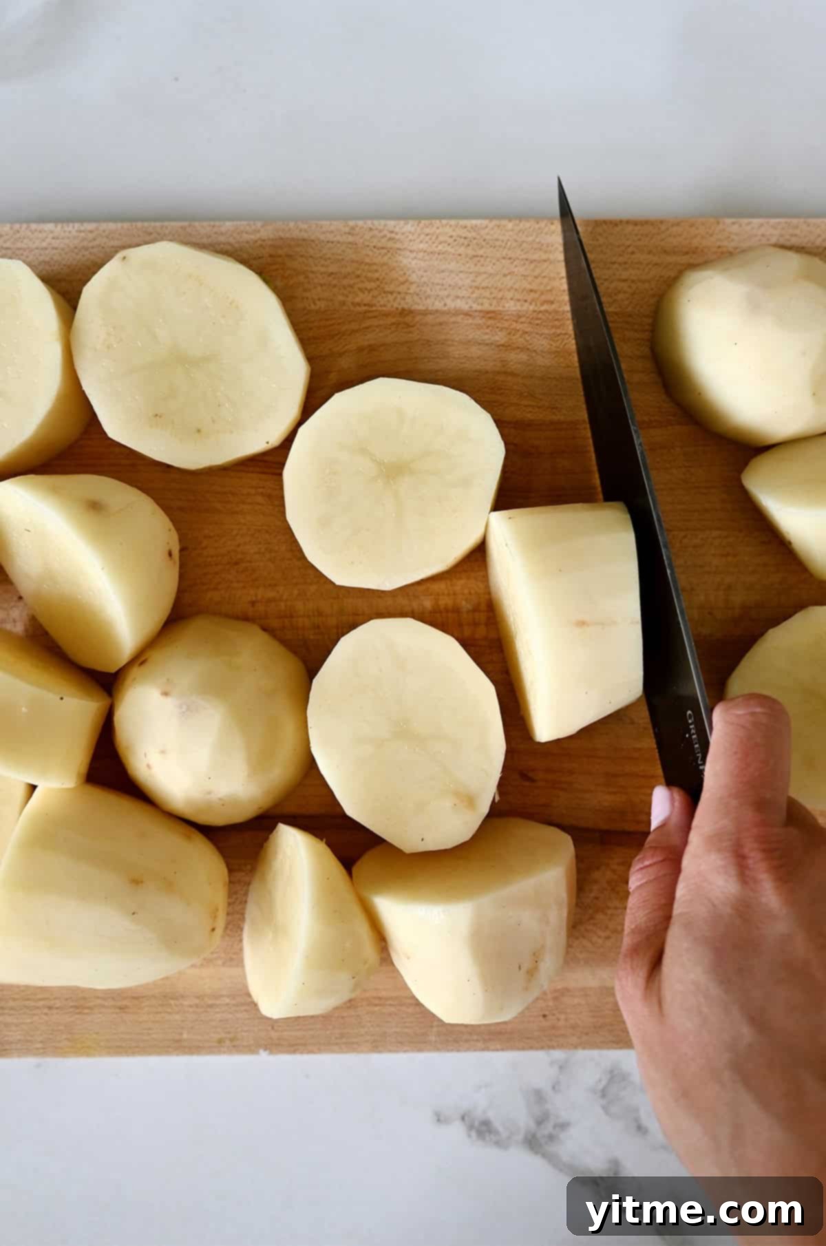 Peeled russet potatoes cut into quarters on a wooden cutting board.