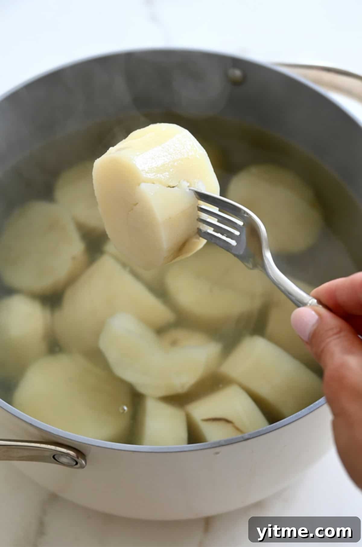 Fork piercing a boiled potato to demonstrate its fork-tender consistency.
