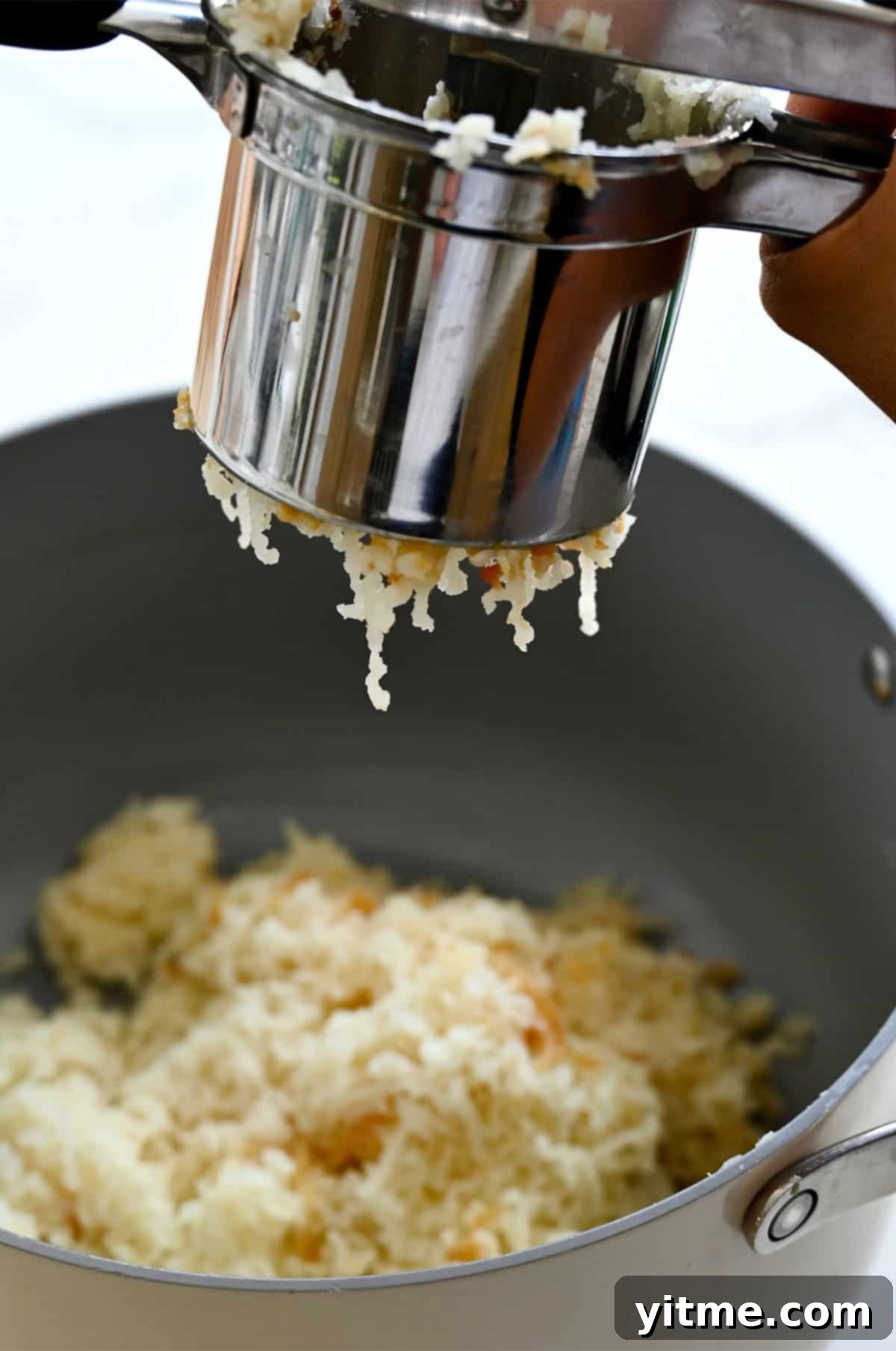 Passing boiled potatoes through a ricer for extra creamy mashed potatoes.