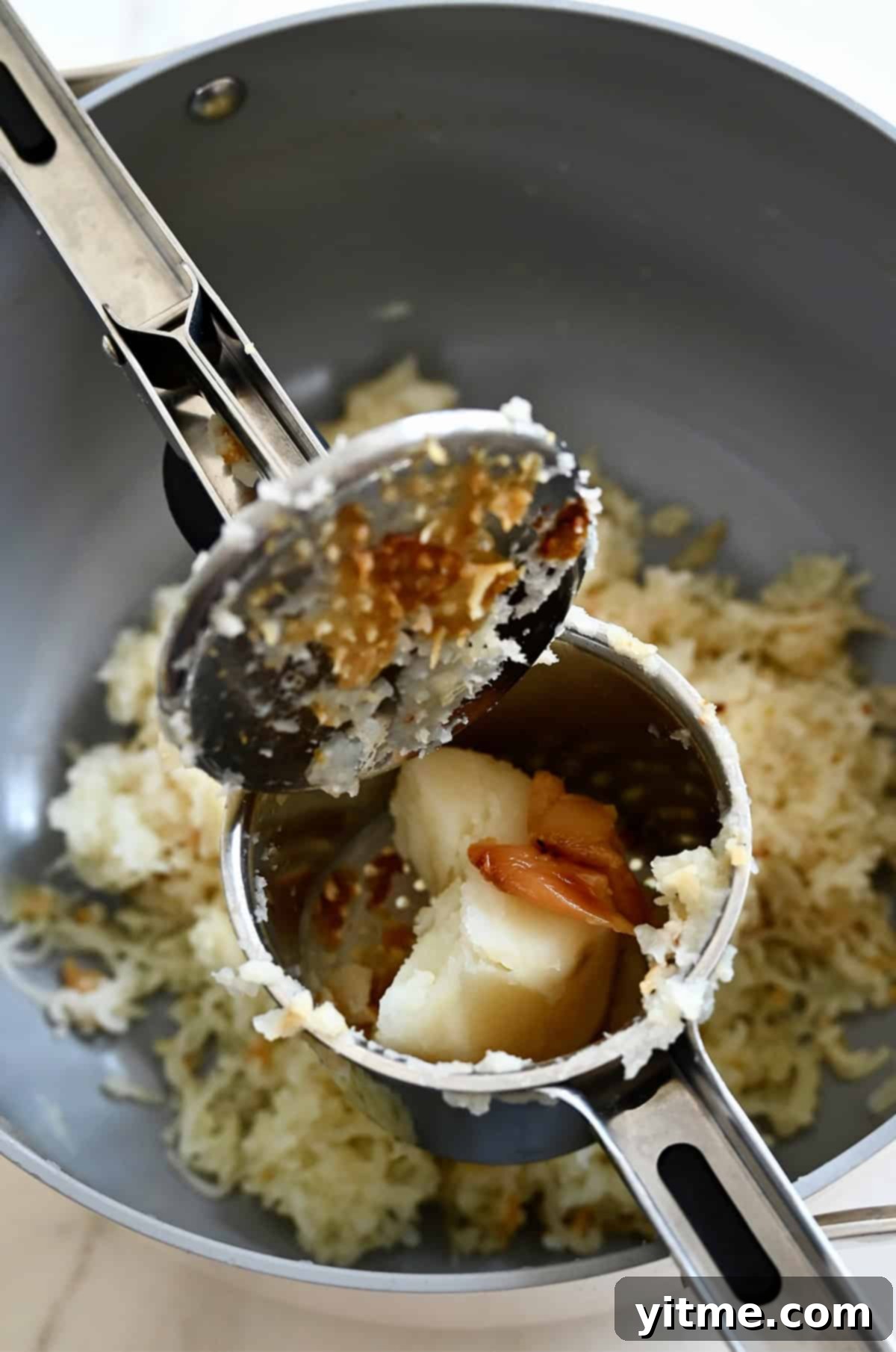 Passing roasted garlic through a ricer, along with boiled potatoes, to create roasted garlic mashed potatoes.