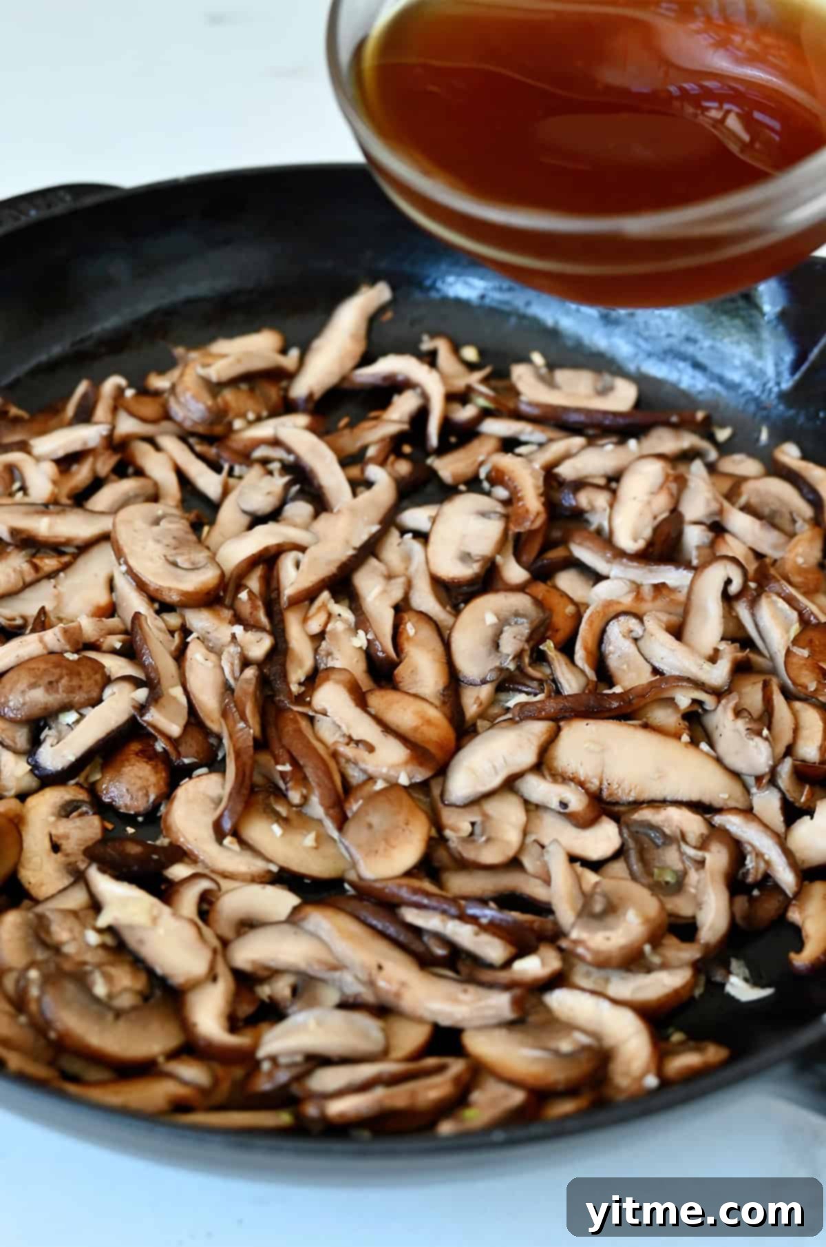 Adding beef stock to sautéed mushrooms and garlic.