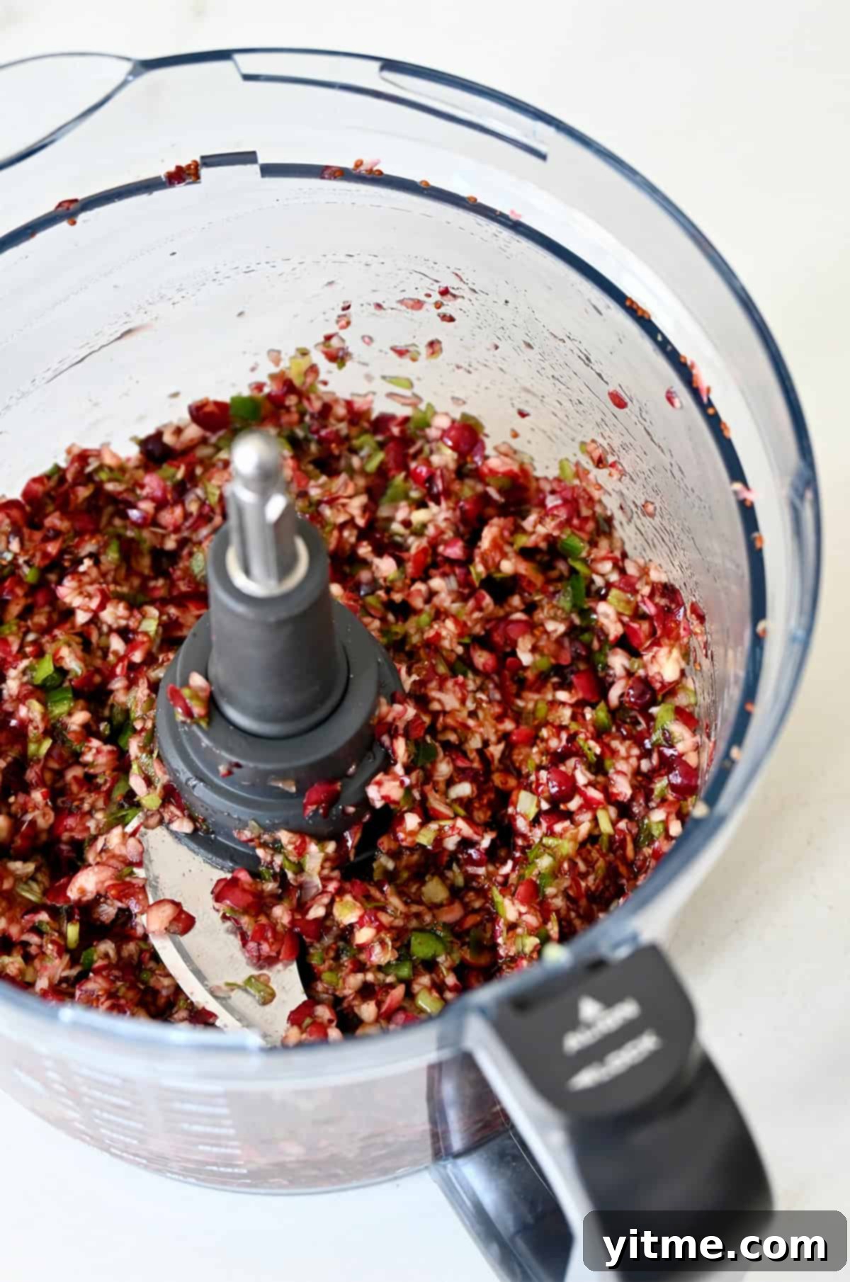 A vibrant cranberry jalapeño relish in a food processor, ready to be chilled and served over cream cheese.