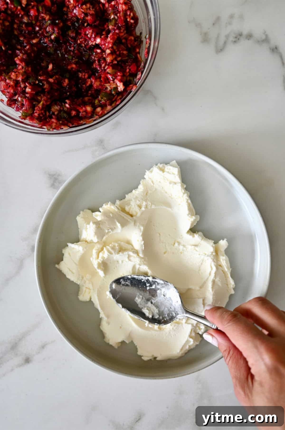 Spreading softened cream cheese with the back of a spoon onto a serving plate, the base for the cranberry jalapeno dip.