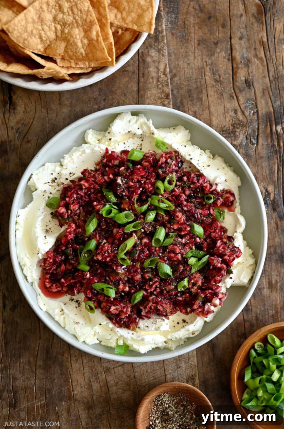 Cranberry jalapeño relish over cream cheese on a serving plate garnished with chopped scallions, salt and pepper, the finished holiday appetizer.
