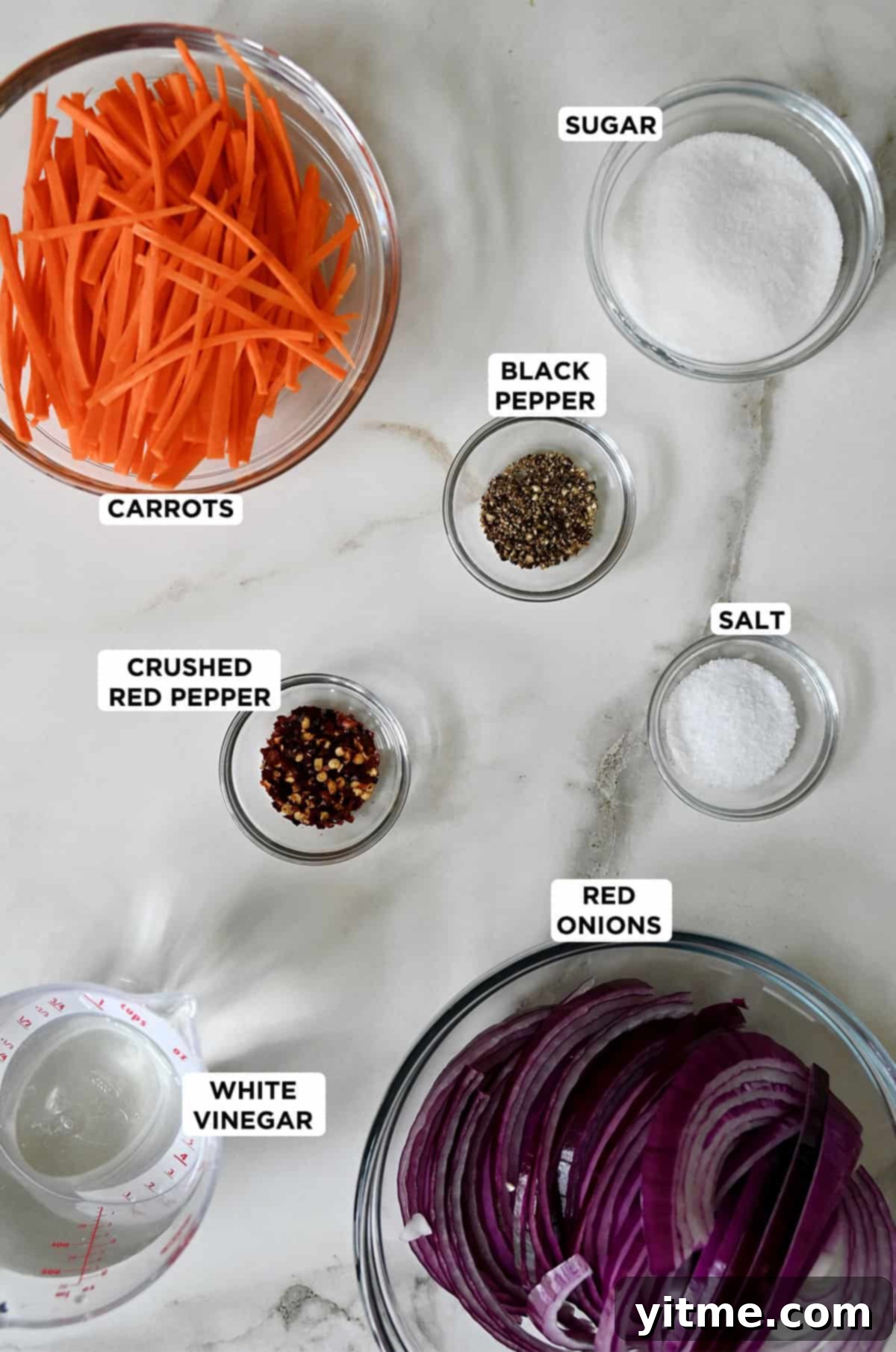 Clear glass bowls are filled with the vibrant ingredients needed to make pickled red onions and carrot relish, showcasing red onions, diced carrots, white sugar, black pepper, pickling salt, crushed red pepper flakes, and clear white vinegar, all neatly arranged on a white surface.