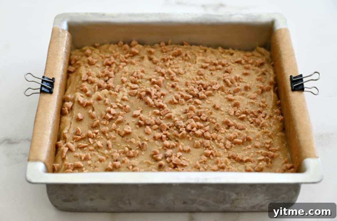 Blondie batter, smoothed evenly into a parchment paper-lined baking pan and secured with metal clips, ready for the oven.