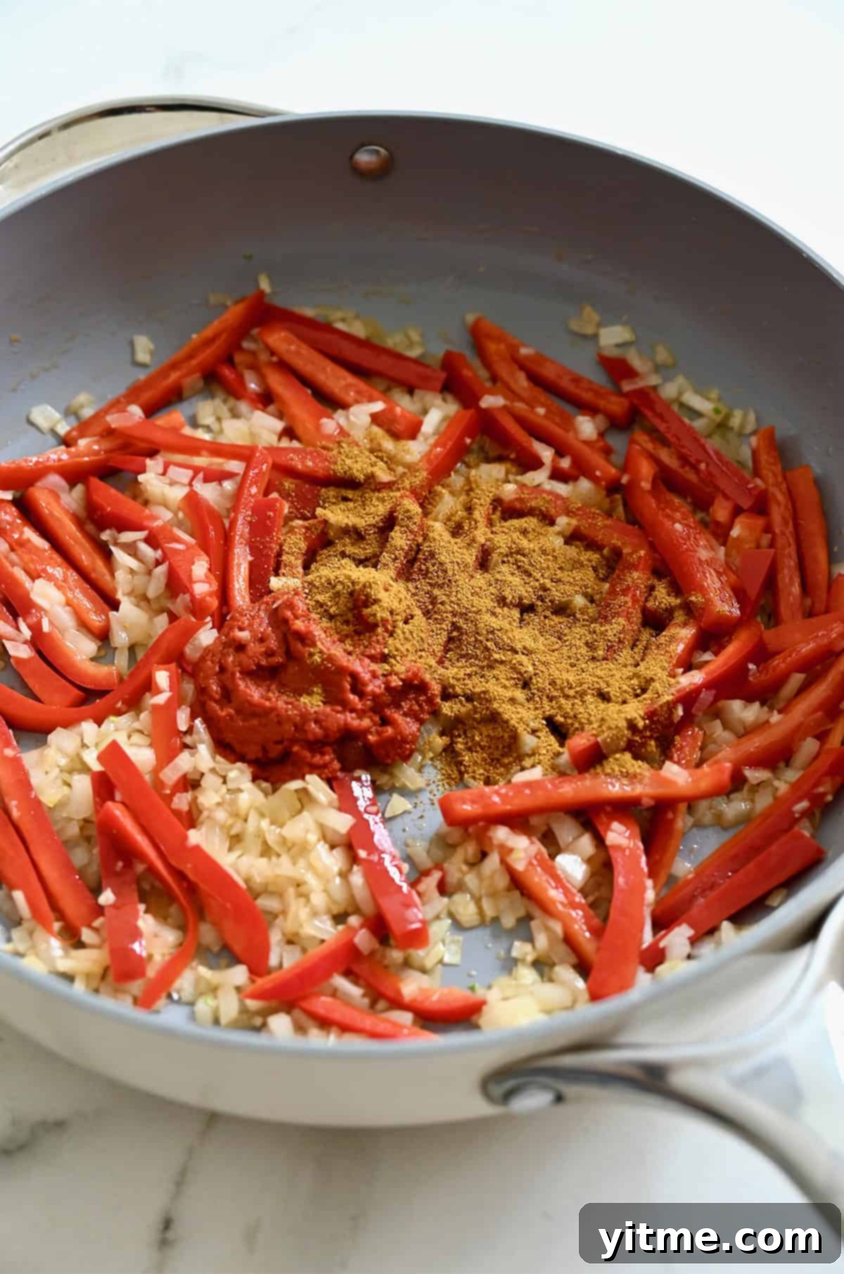 Red curry paste and yellow curry powder atop sautéed aromatics in a large skillet.