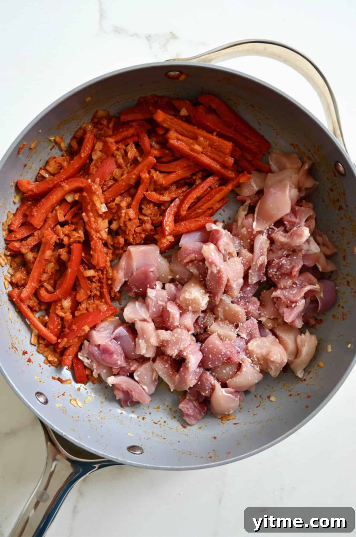 Diced chicken thighs in a skillet with curried vegetables.