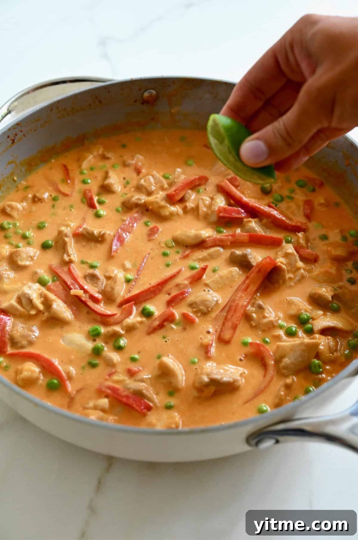 Squeezing a lime to add its juice to coconut chicken curry in a pan.