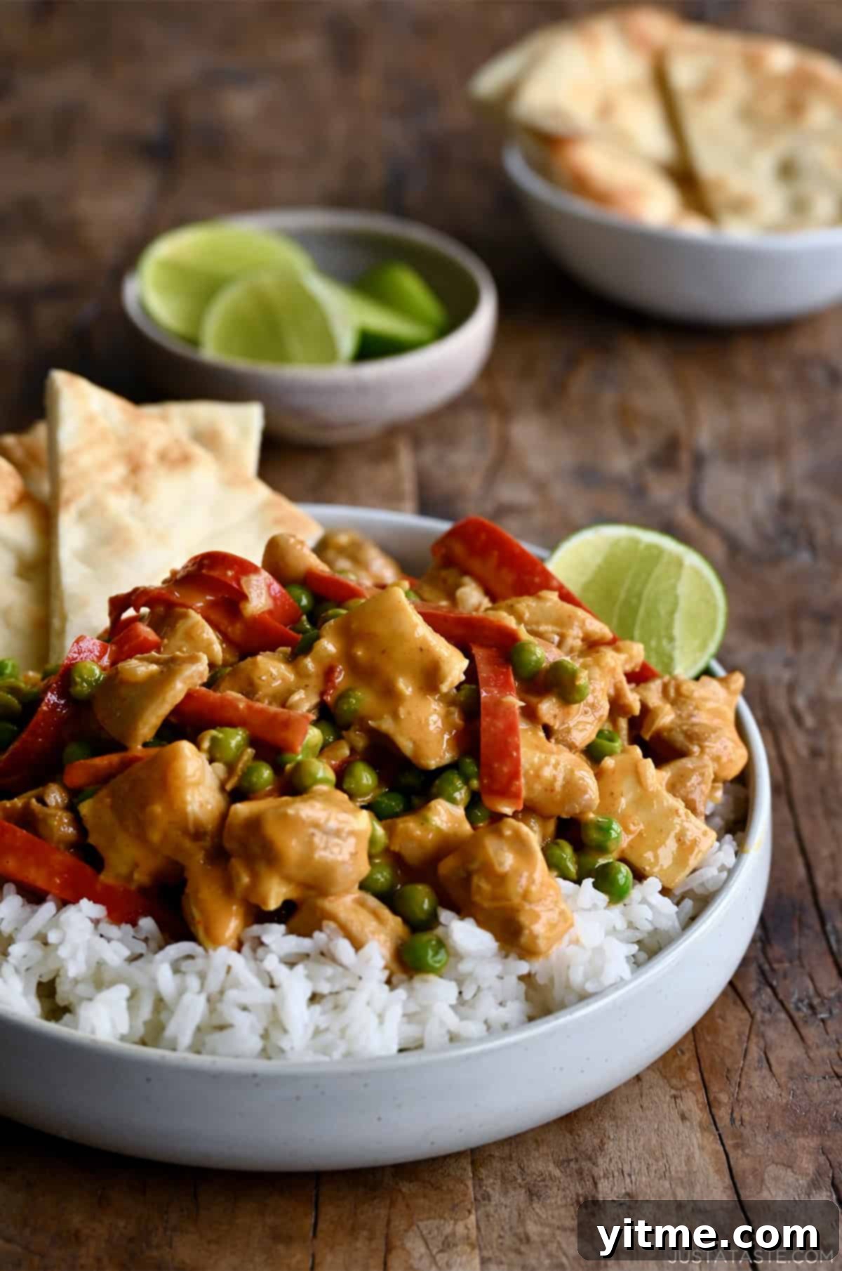 Coconut curry chicken with peas and bell peppers served with basmati rice, naan, and a lime wedge.