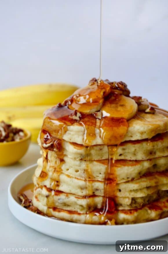 Fluffy Banana Nut Pancakes 2 A tall stack of banana pancakes topped with bananas and maple syrup