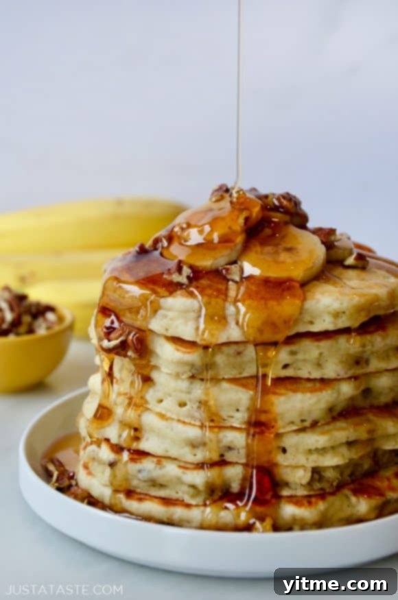 Fluffy Banana Nut Pancakes 4 Stack of Banana Nut Pancakes topped with fresh banana slices, pecans and maple syrup; bananas and small bowl with pecans in background