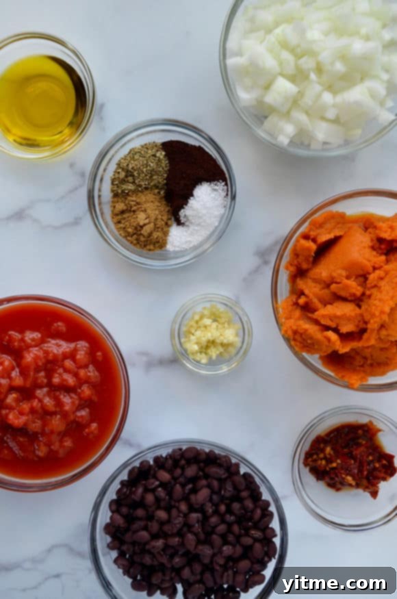 Glass bowls containing various ingredients for pumpkin chili. Fresh vegetables, spices, and ground turkey are ready to be cooked.