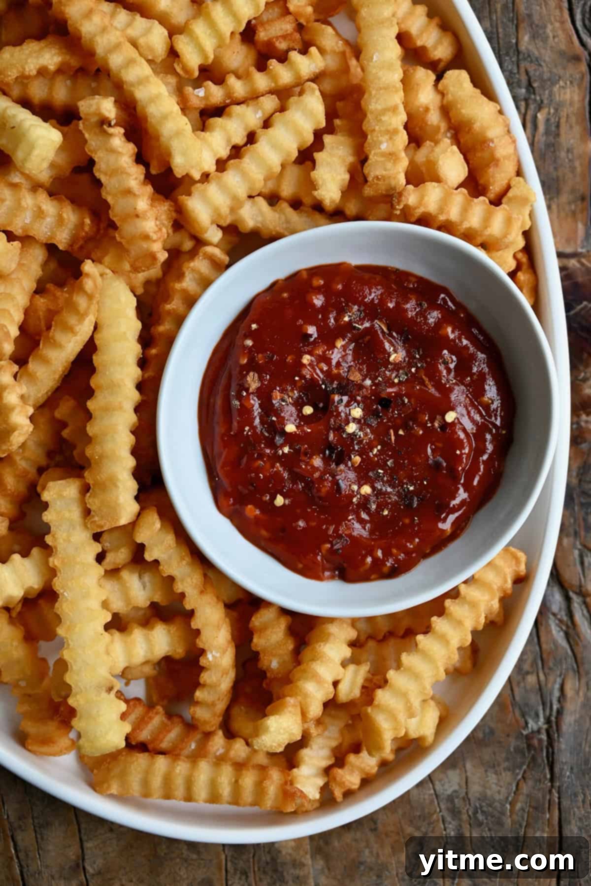 A white bowl of spicy ketchup served with crispy crinkle-cut French fries.