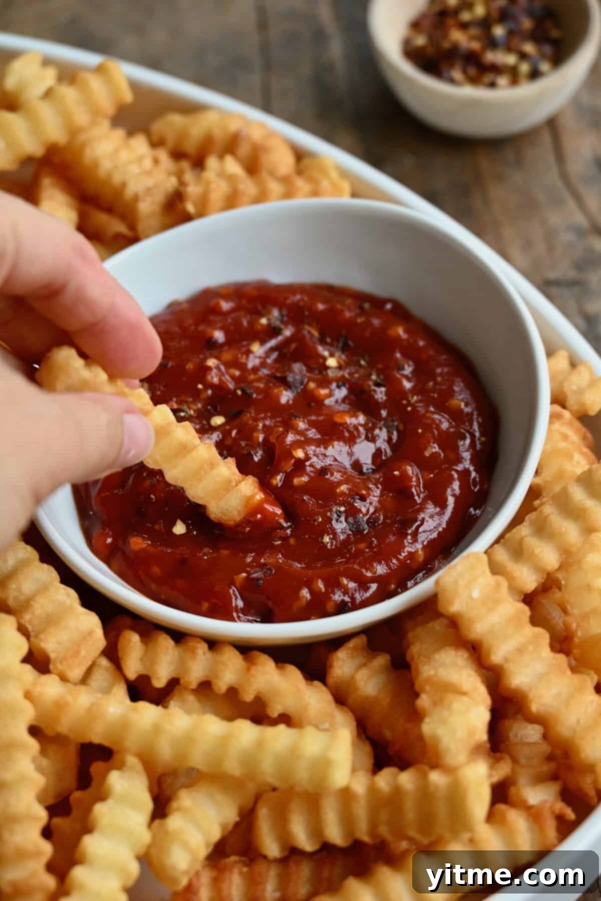A hand dipping a French fry into spicy ketchup.