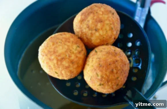 Arancini rice balls being removed from hot oil with a slotted spoon