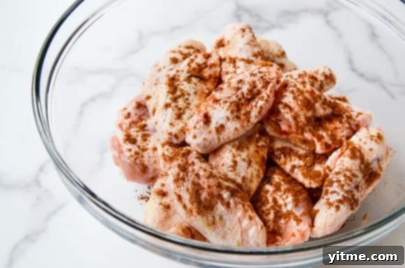 Unbaked chicken wings with seasoning in a clear bowl