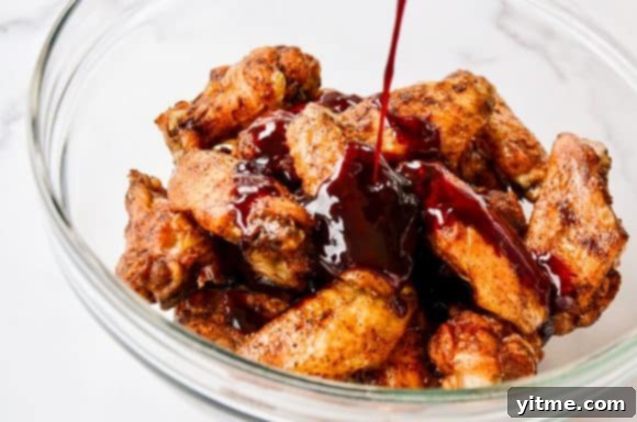 Drizzling sauce over chicken wings in a bowl