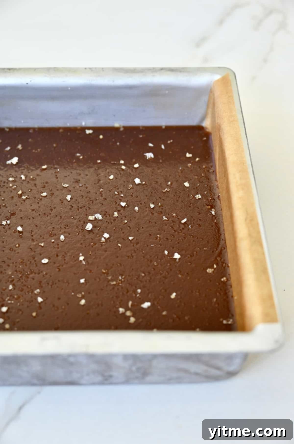 Homemade soft caramels topped with large-flake sea salt in a pan lined with parchment paper.
