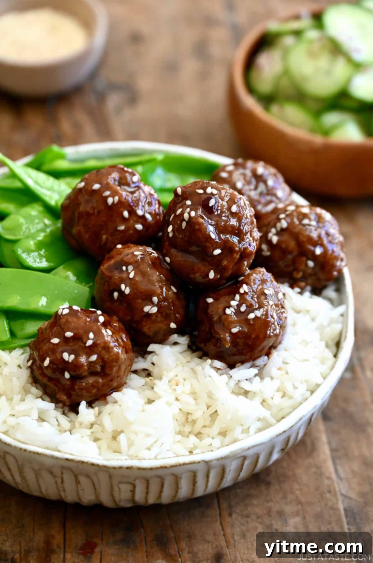 Blackberry jam meatballs garnished with sesame seeds atop white rice in a bowl with snap peas.