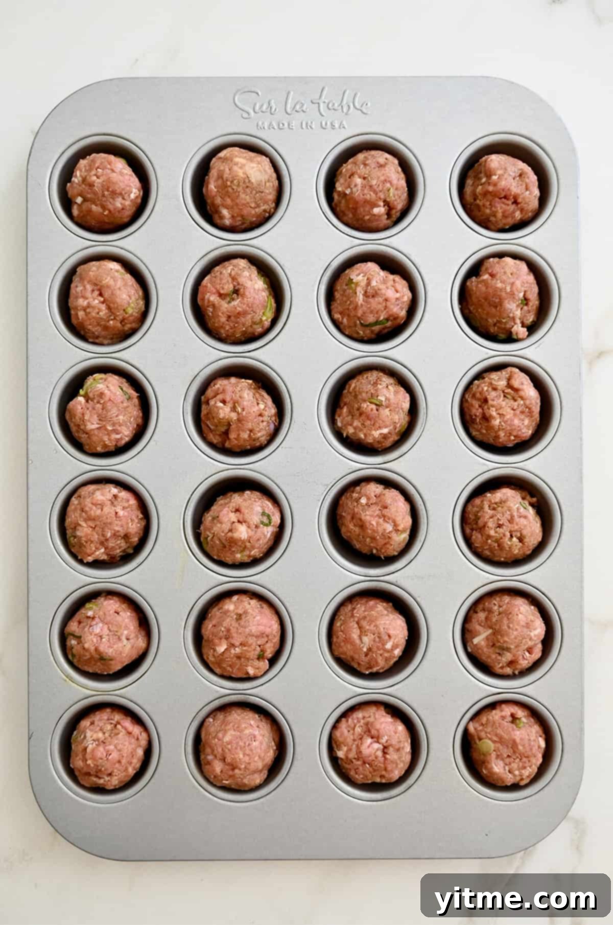 Unbaked meatballs in a mini muffin pan.